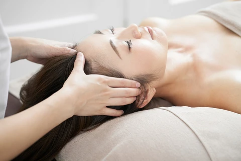 Hands gently massaging the head during a scalp care session